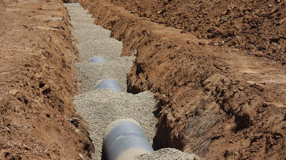 Perforated pipe laid on gravel in an open trench, similar to septic drain field repair work