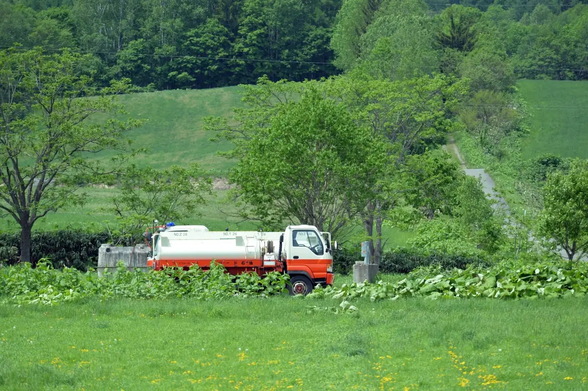 Tank truck parked beside a green field on a rural road